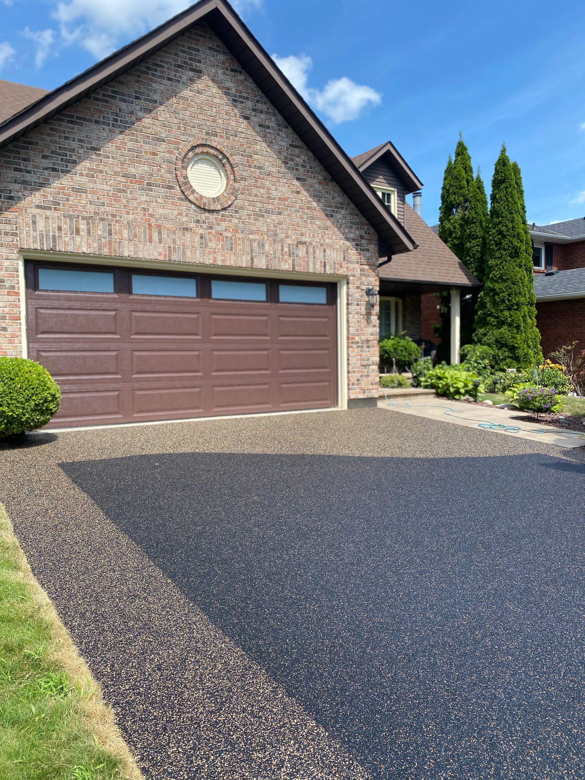 Brown brick house with brown garage door and black pebbled driveway.