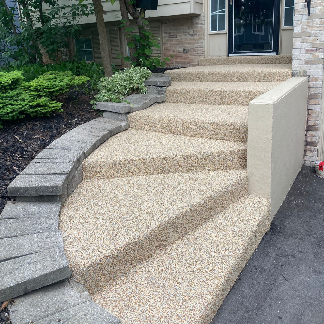 Stone steps leading to a house entrance. Tan speckled surface, curved design, dark door.