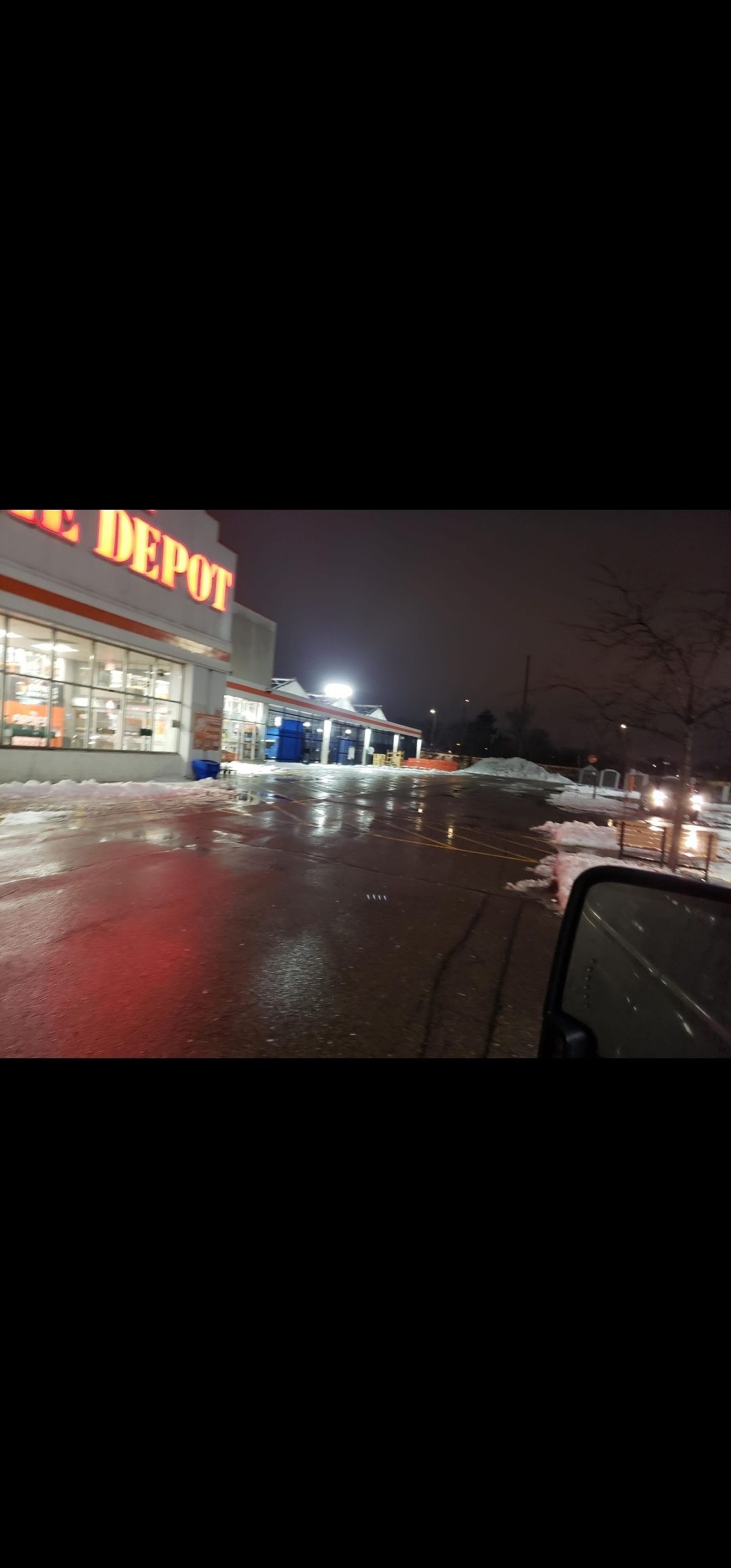 A car is parked in front of a home depot at night.