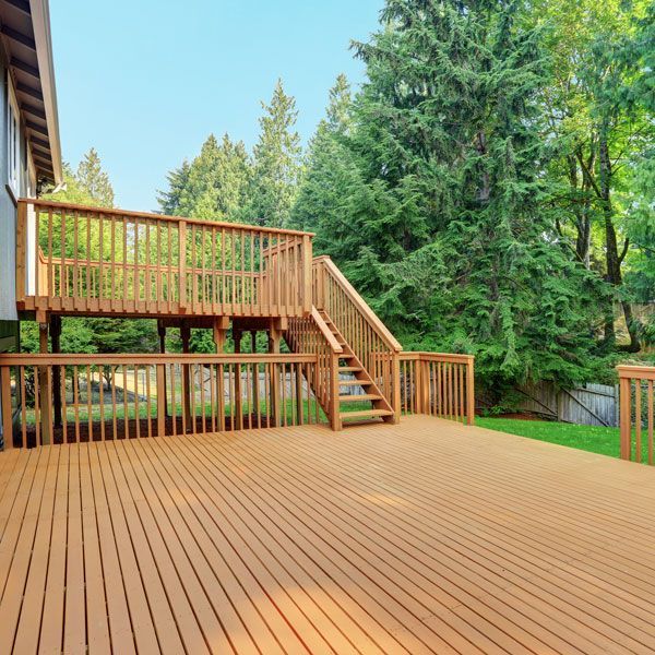 Wooden deck with stairs, surrounded by a wooden railing, and a large tree in the background.