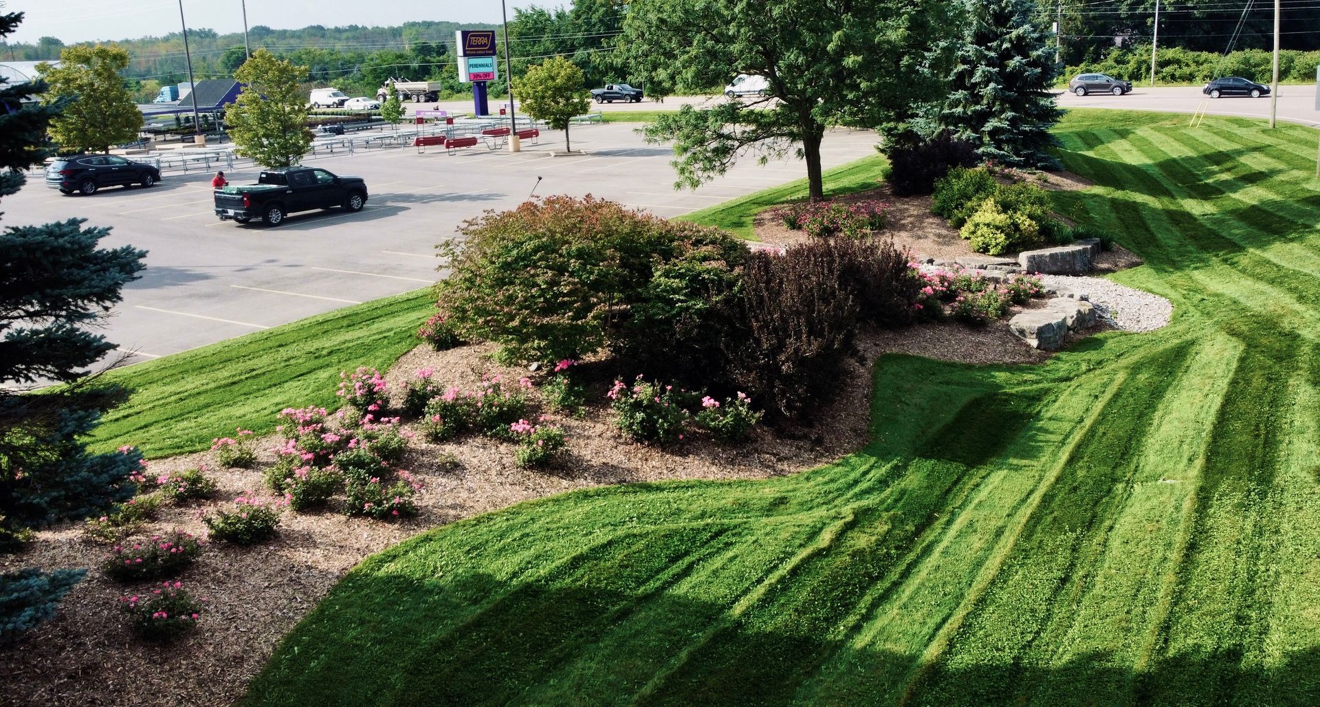 Lush green lawn with landscaping in front of a parking lot and road.