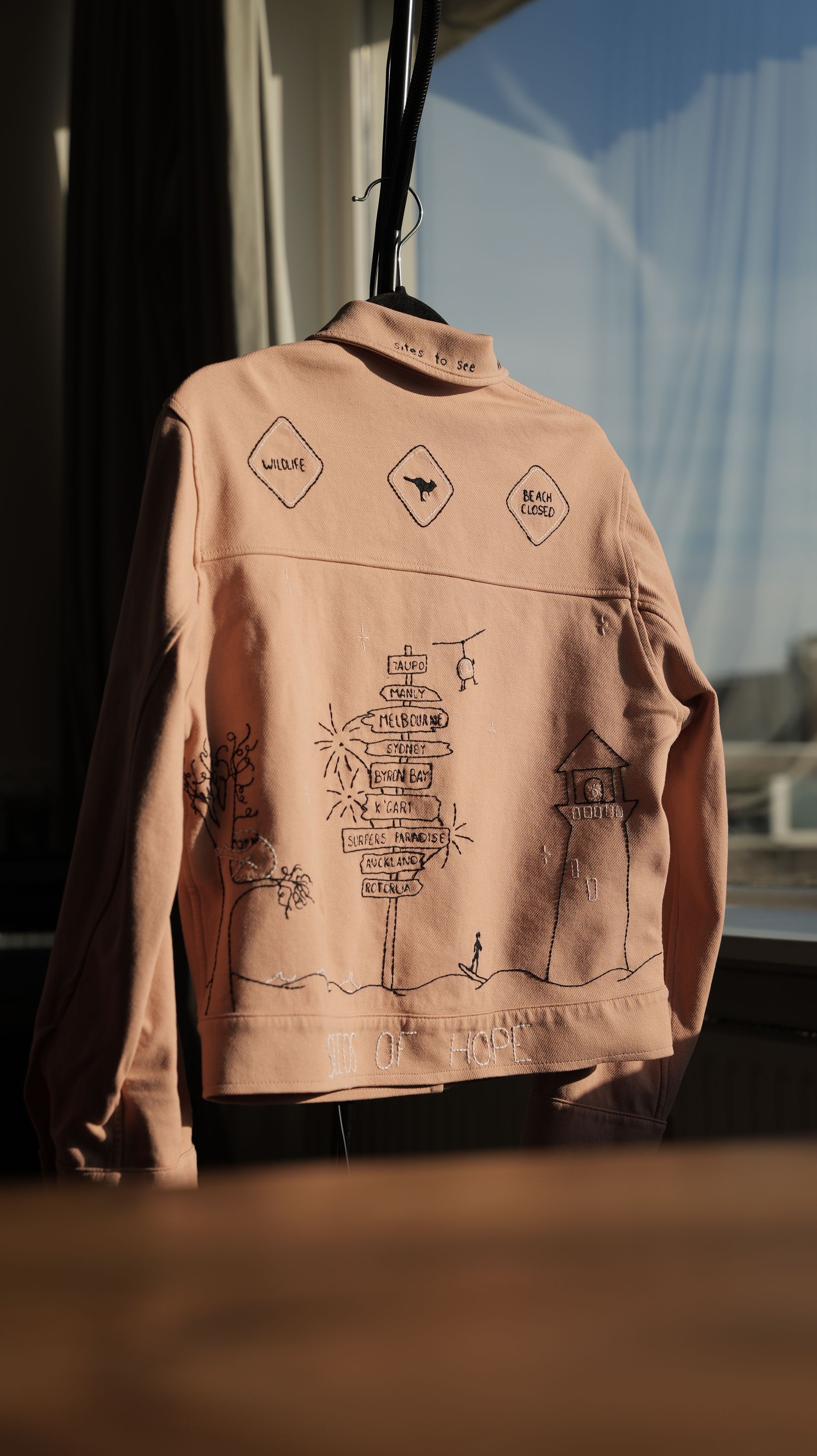 Roze spijkerjas met zwarte handgeborduurde figuren van een reis door Australië.