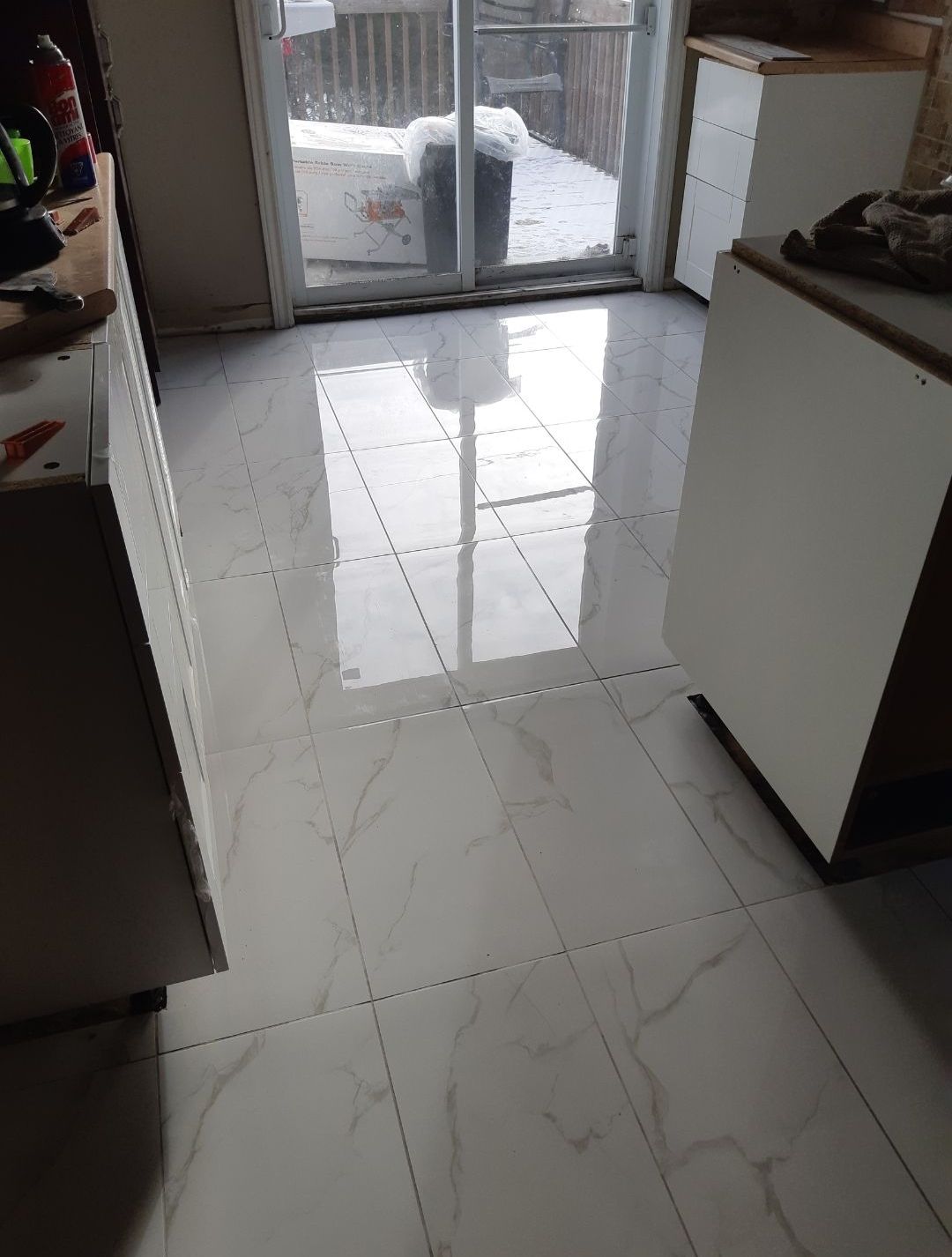 Une cuisine avec carrelage blanc et porte coulissante en verre.