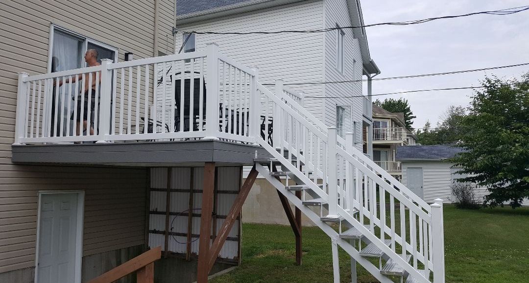 Une terrasse blanche avec des escaliers qui y mènent se trouve sur le côté d'une maison.