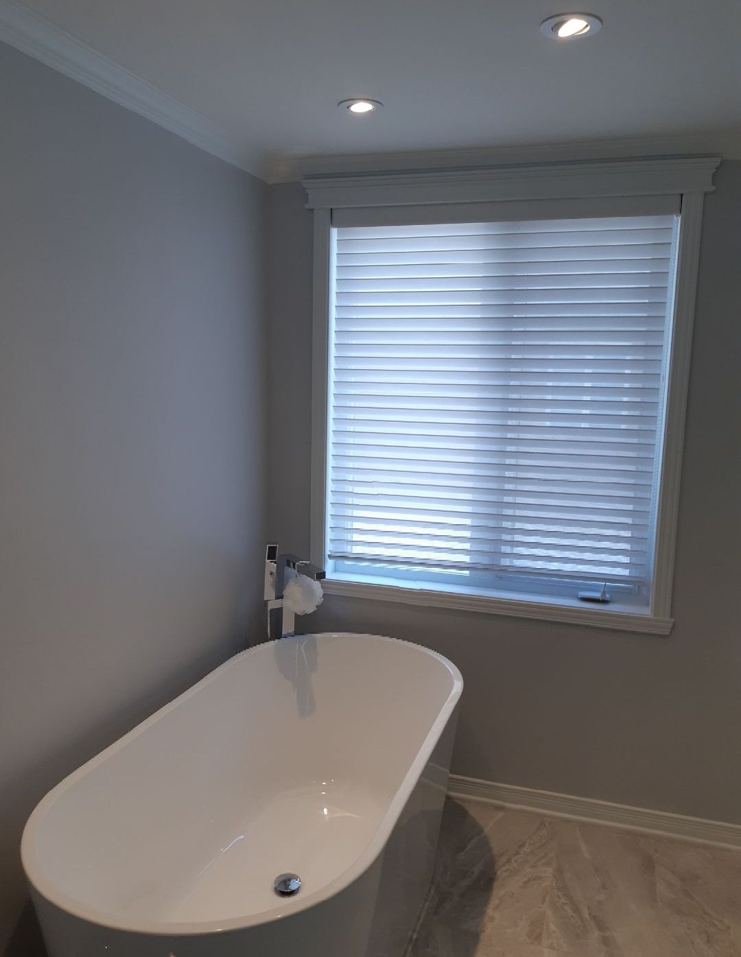 Une salle de bain avec baignoire et une fenêtre avec stores.