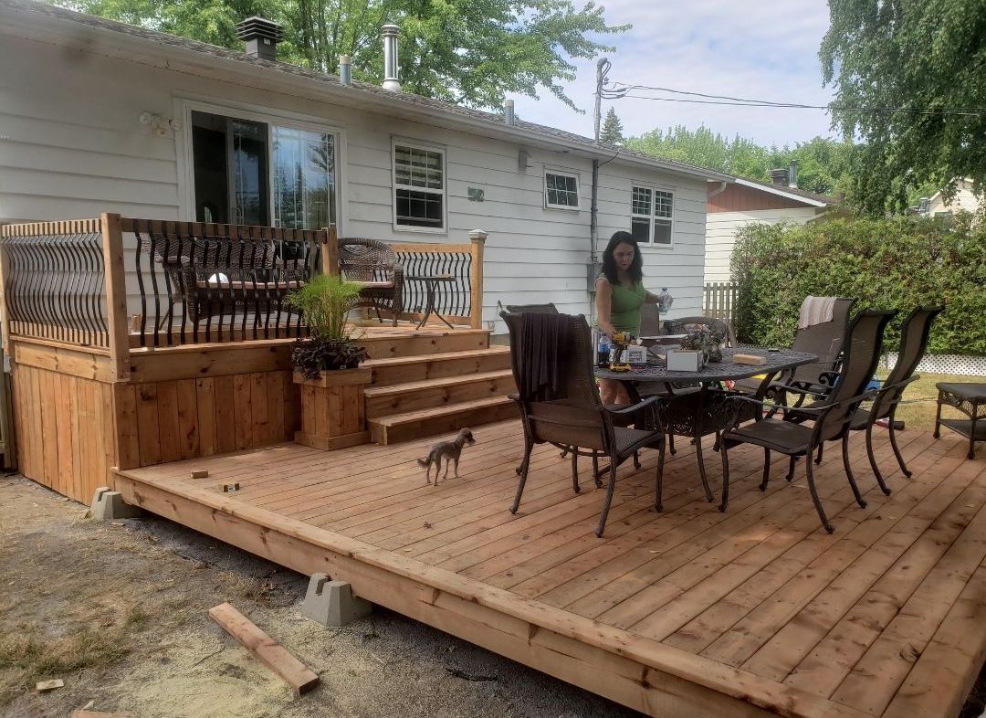 Une femme est debout sur une terrasse en bois avec une table et des chaises.