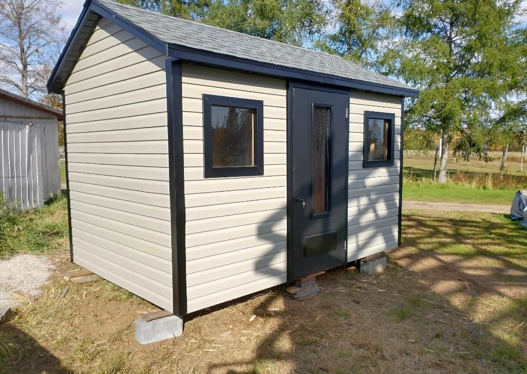 Un petit hangar blanc avec des garnitures noires est posé au sommet d'un champ de terre.