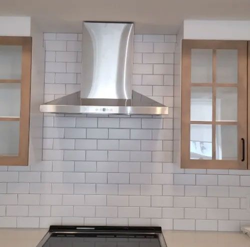 Une hotte en acier inoxydable est montée sur un mur de briques blanches dans une cuisine.