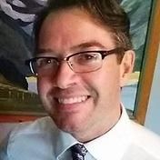 Man with glasses smiling, wearing a white shirt and tie.