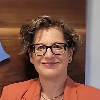 Woman wearing glasses and a coral blazer smiling, indoors.