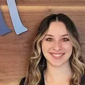 Woman with wavy blonde hair smiling in front of a wood background with a blue shape.