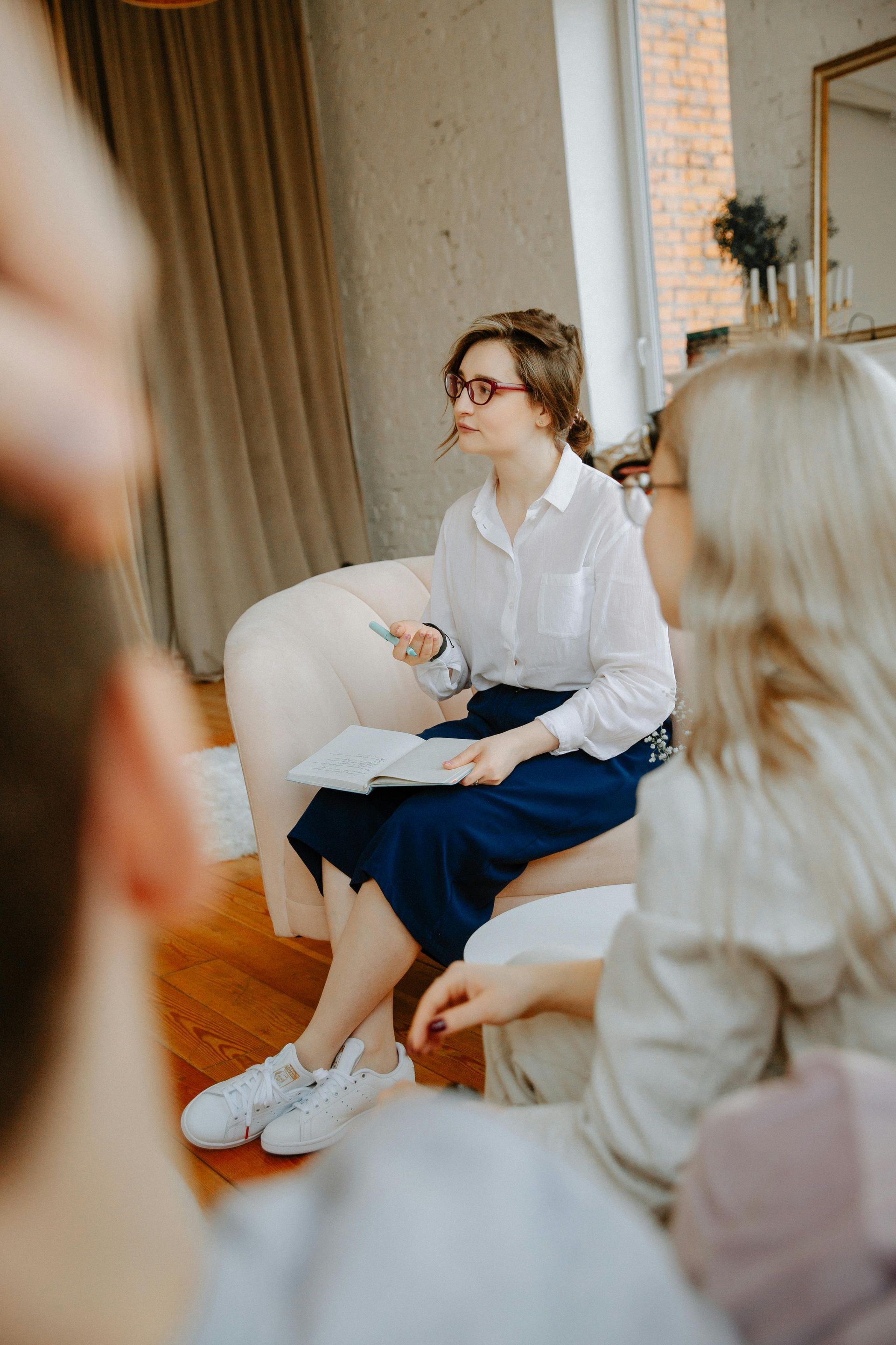 Seated speaker in white blouse and blue skirt addresses a small group in a bright room