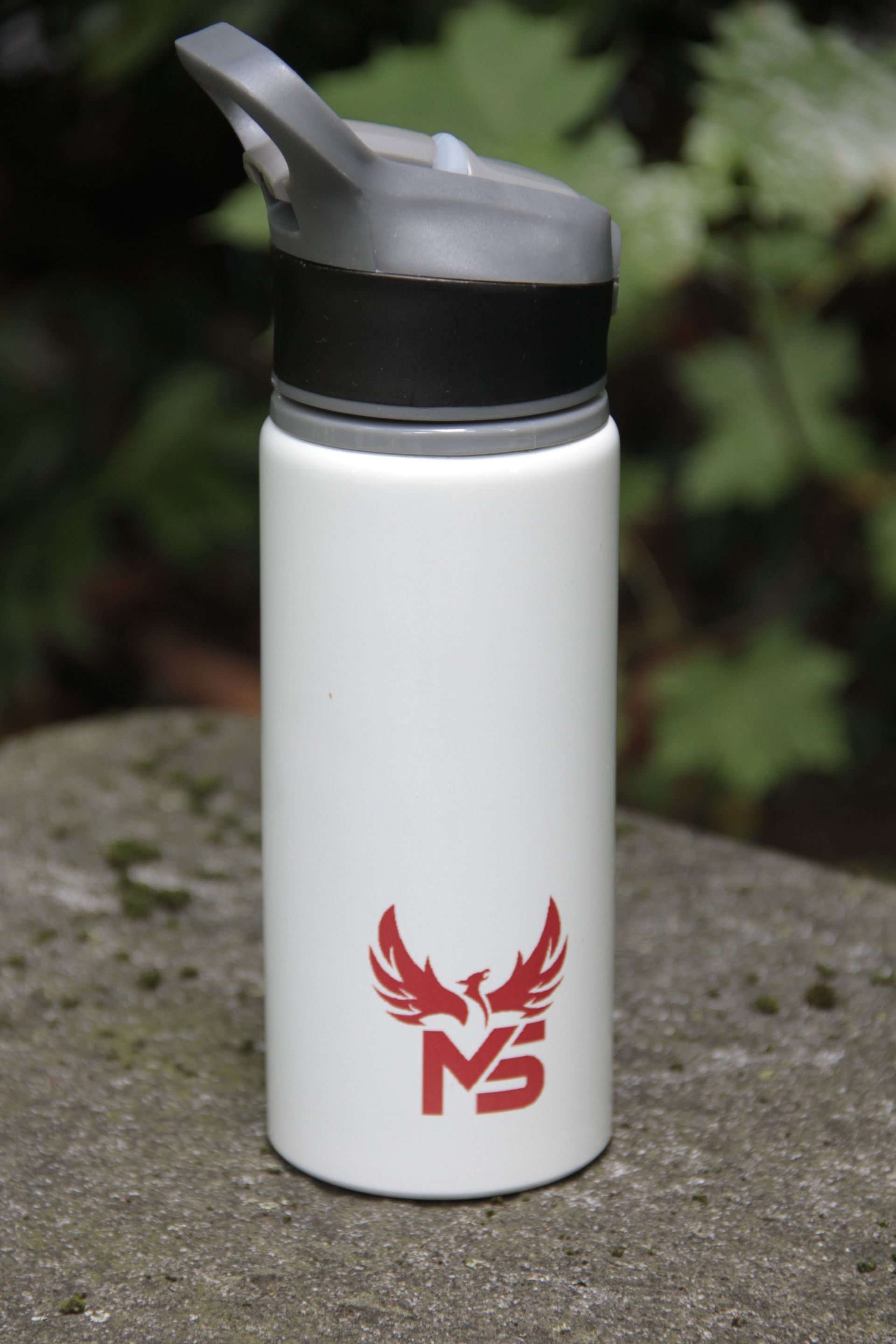Bouteille d'eau blanche avec un bouchon à clapet noir et un logo rouge, posée sur une surface en pierre à l'extérieur.