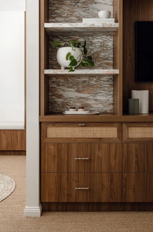 A wooden storage cabinet with a cane drawer front and open shelves styled with decor, plants, and a marble backdrop. — PKJ Design in Unanderra, NSW 