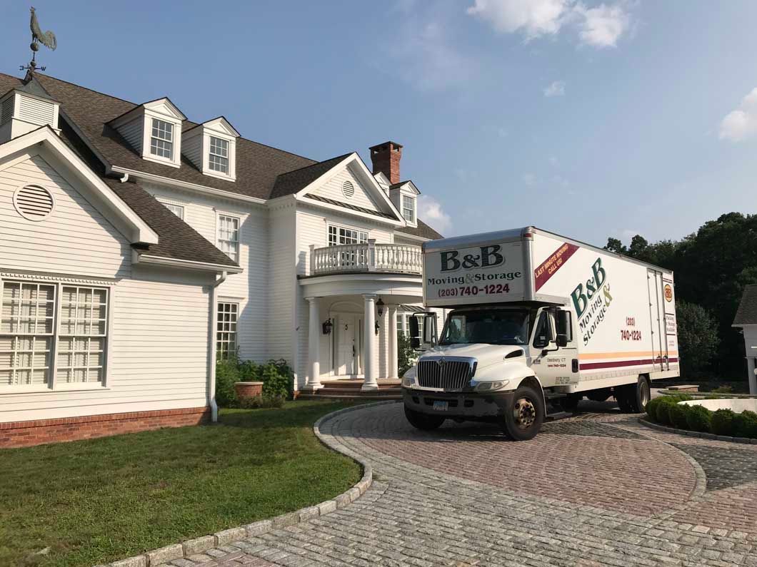 A moving truck is parked in front of a large white house.