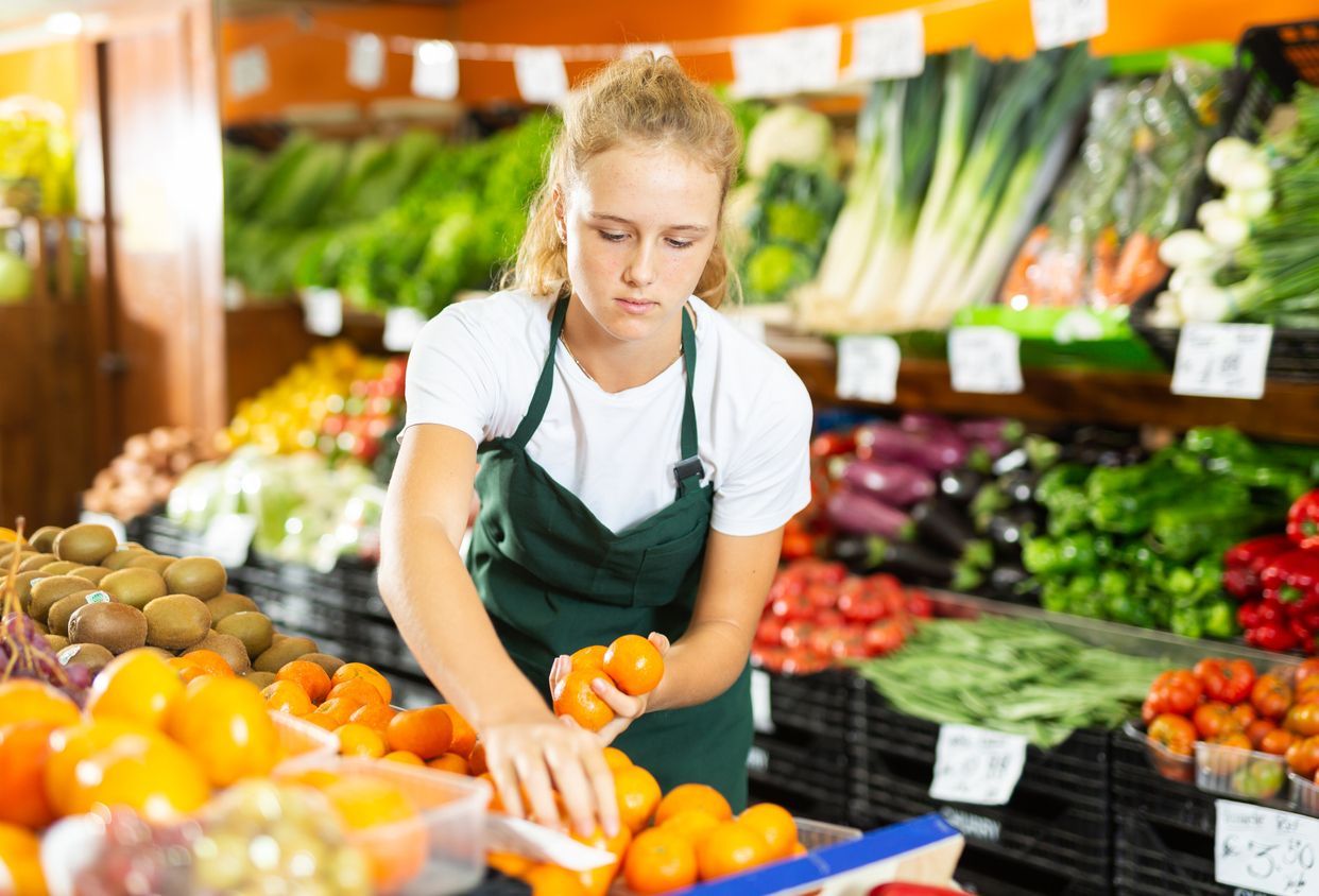 A woman is sorting oranges in a grocery store.