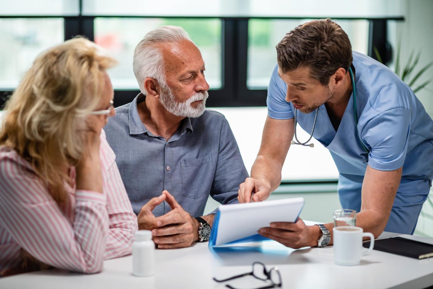 A doctor is talking to an elderly couple while looking at a tablet.