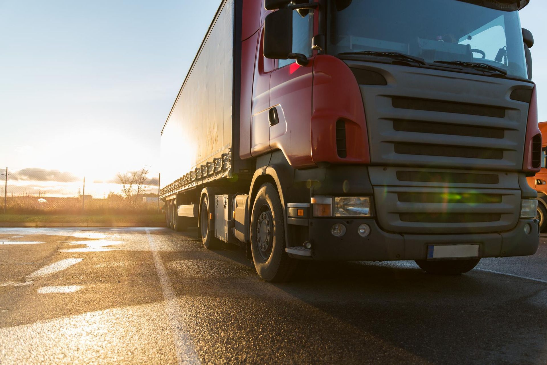 A red semi truck is driving down a wet road at sunset.