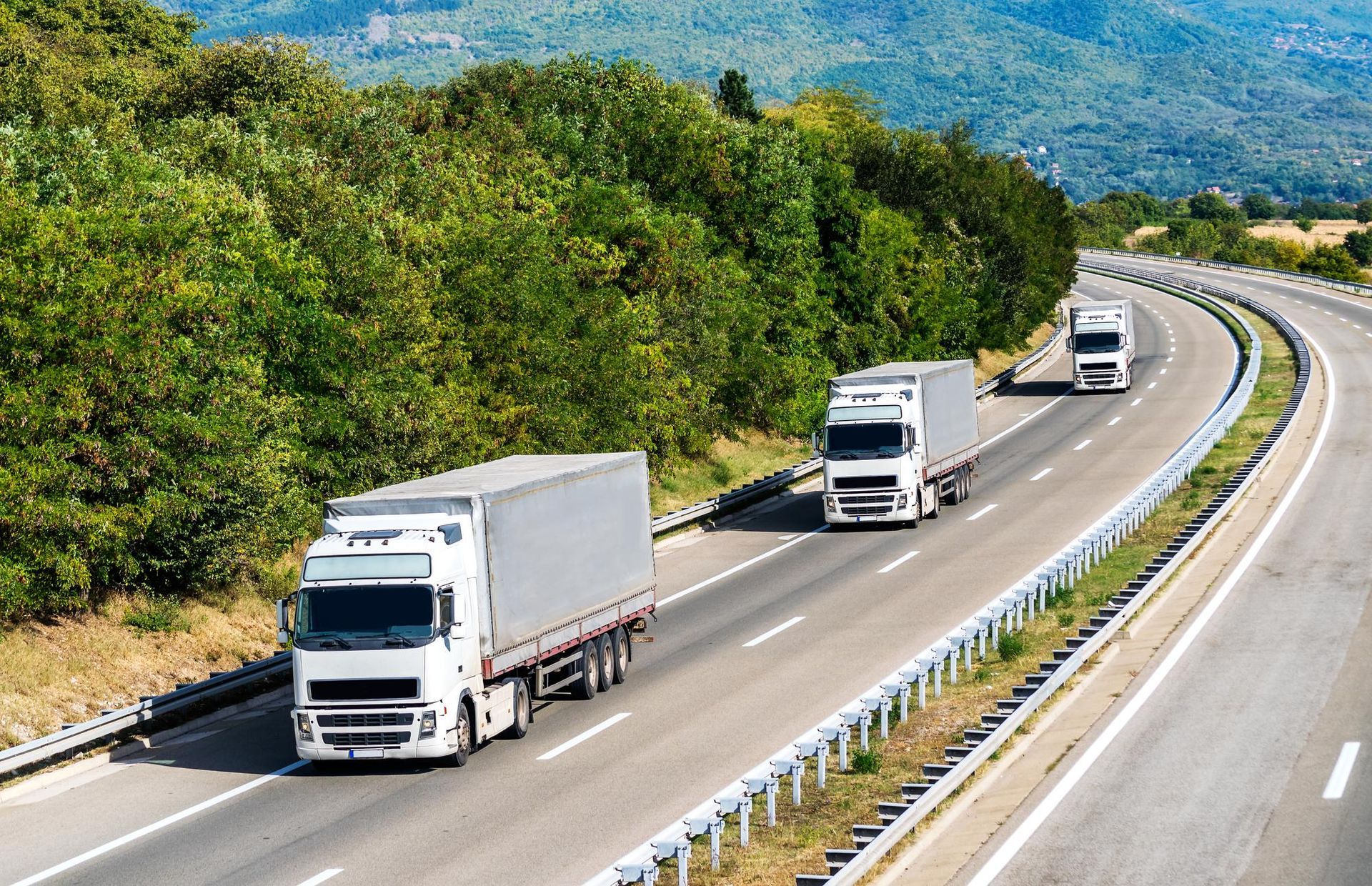 A row of white trucks are driving down a highway.