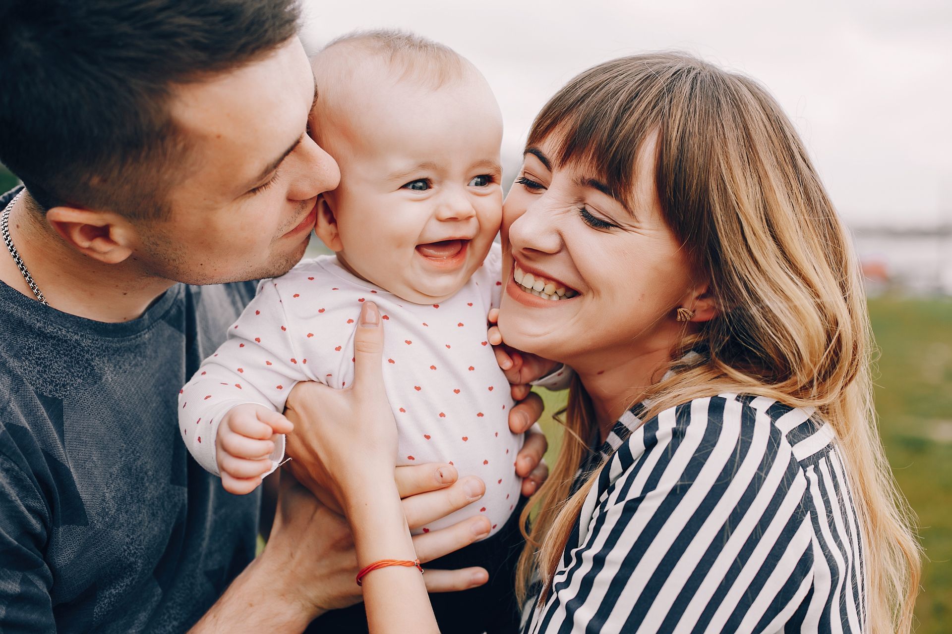 A man and woman are kissing a baby on the cheek.
