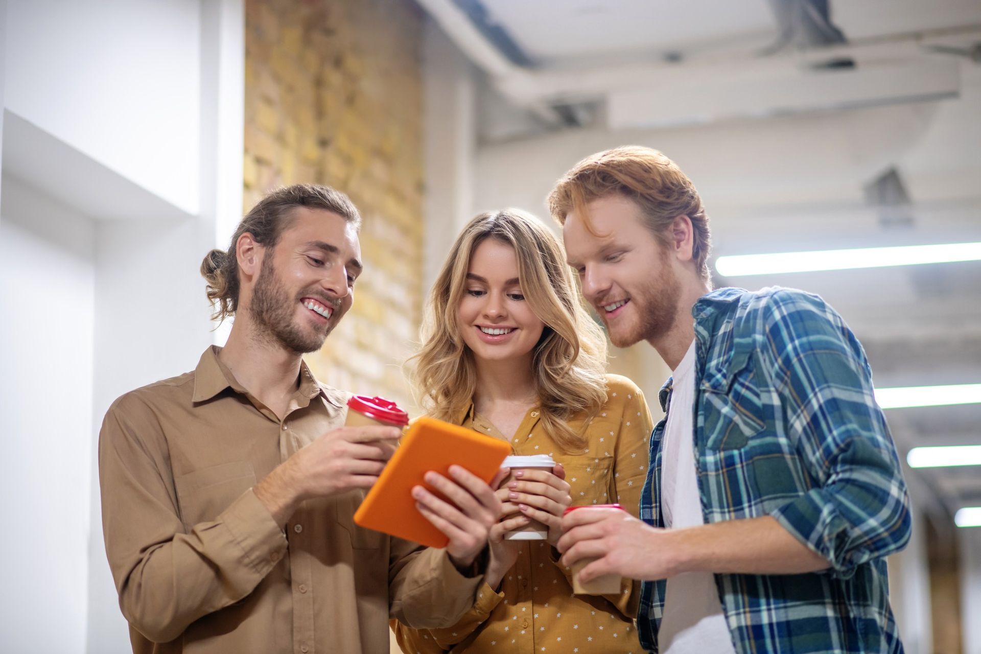 A group of people are standing in a hallway looking at a tablet.