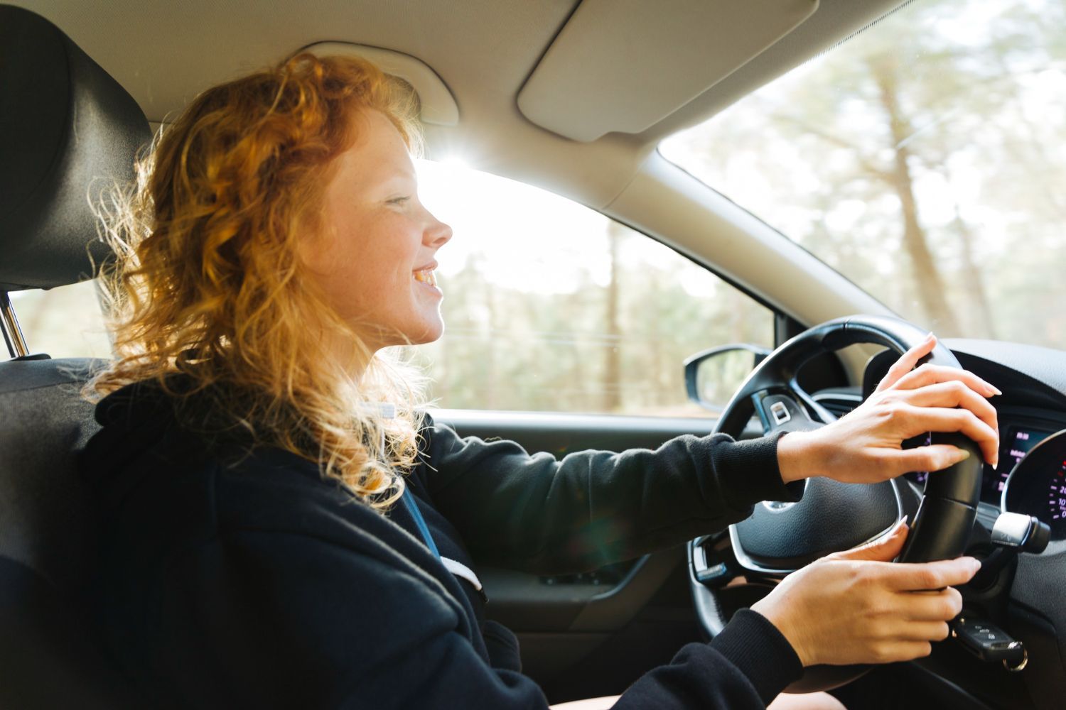 A woman is driving a car with her hands on the steering wheel.