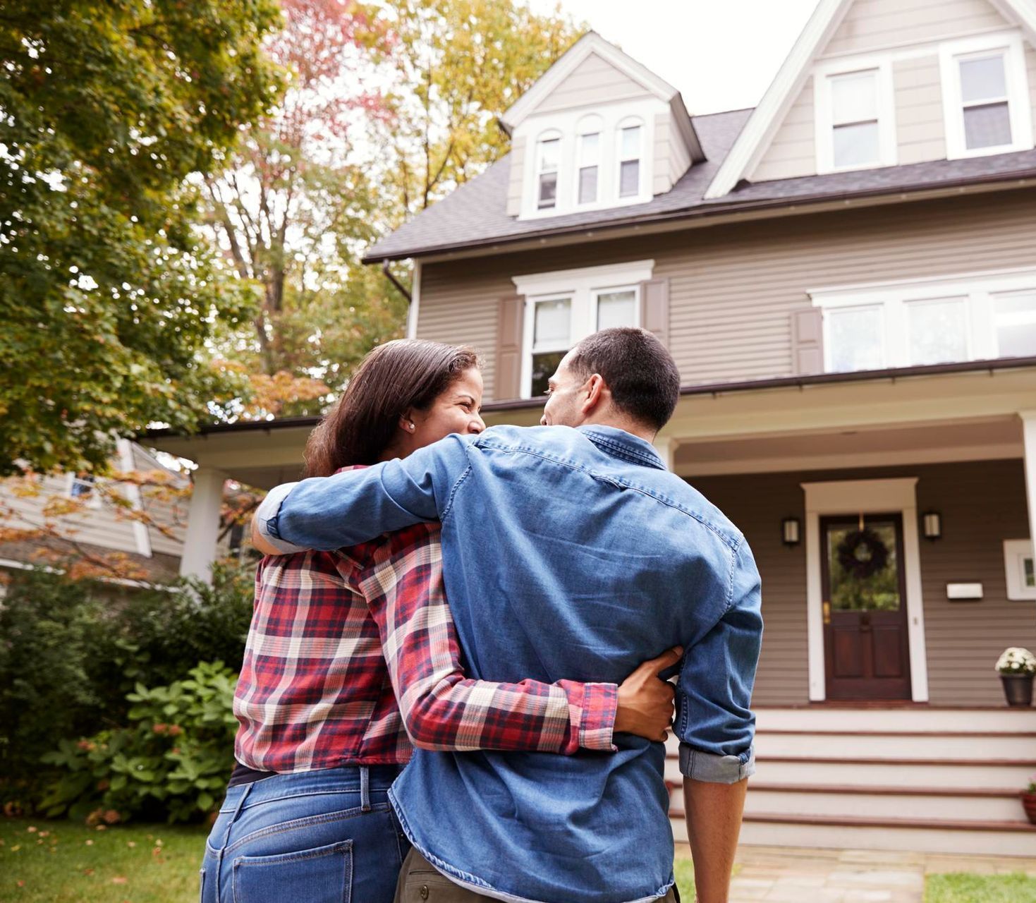 A man and a woman are hugging in front of a house.