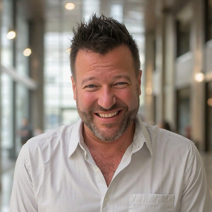 A man with a beard is smiling for the camera while wearing a white shirt.