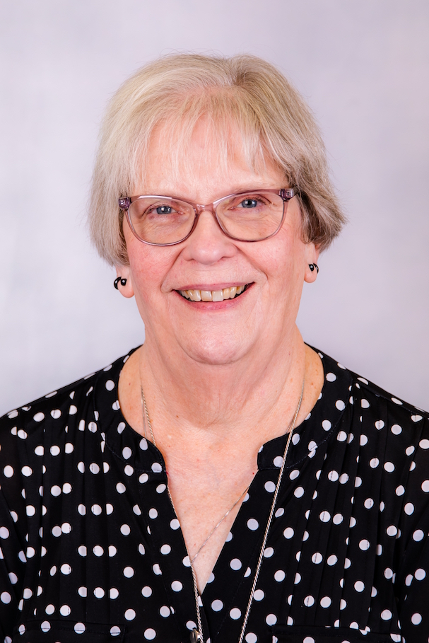 A woman wearing glasses and a black and white polka dot shirt is smiling for the camera.