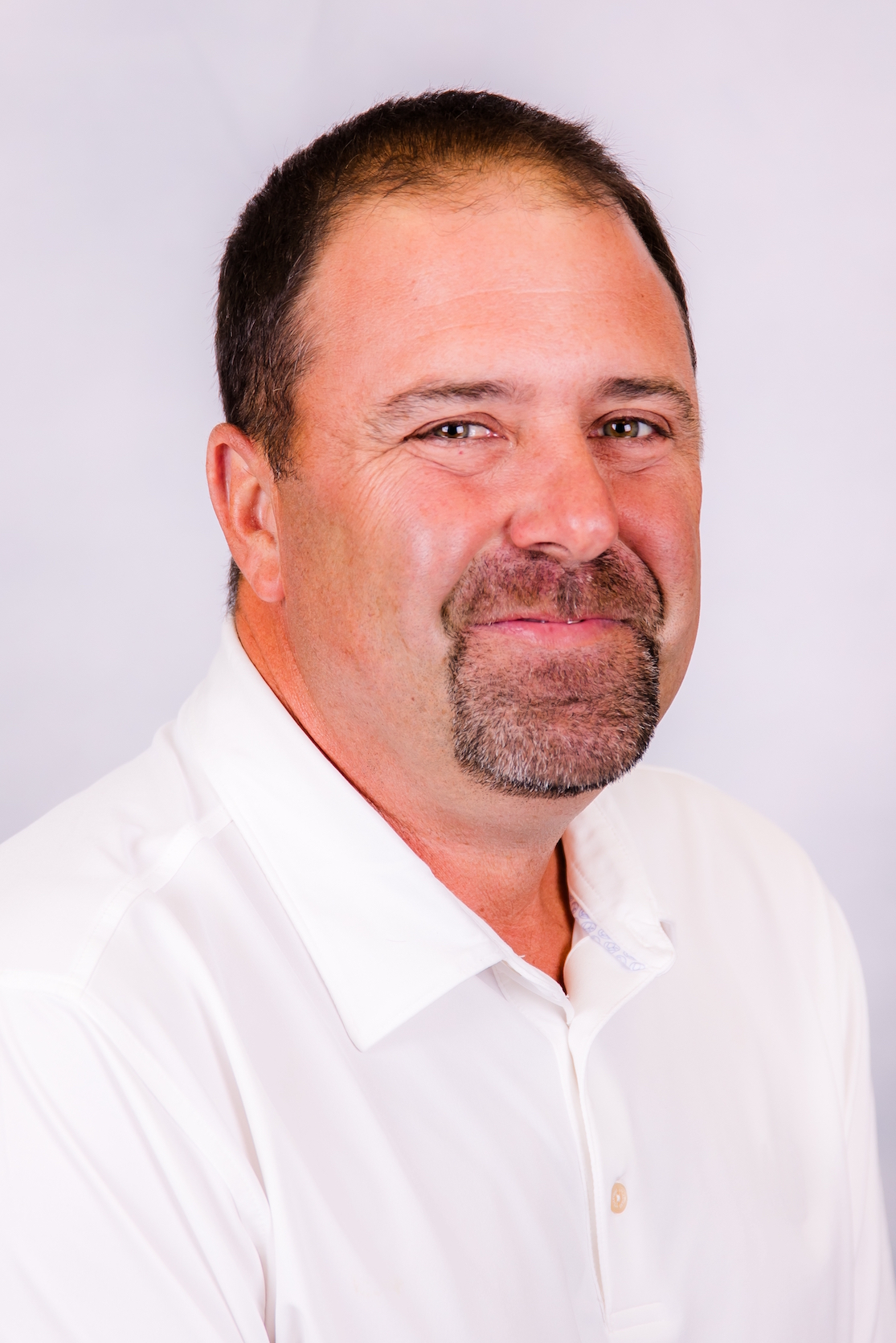 A man with a beard is wearing a white shirt and smiling for the camera.