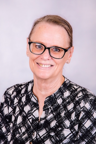 A woman wearing glasses and a plaid shirt is smiling for the camera.