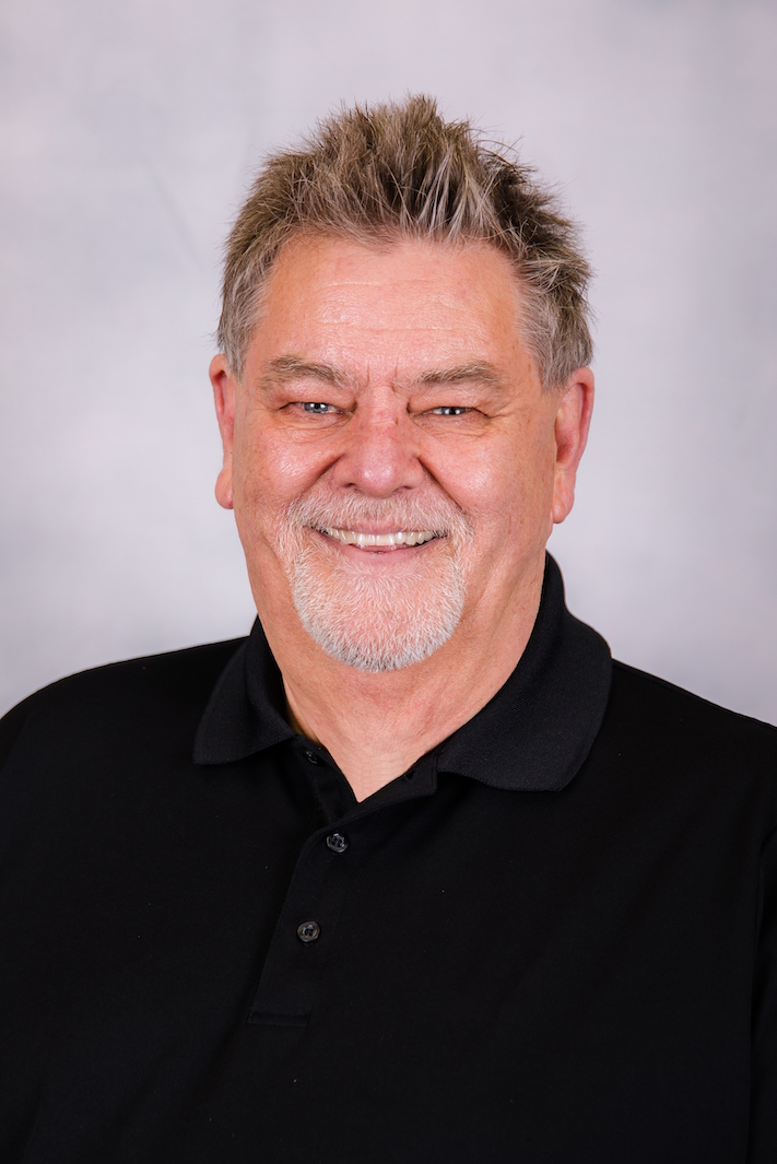 A man with a beard is wearing a black shirt and smiling for the camera.