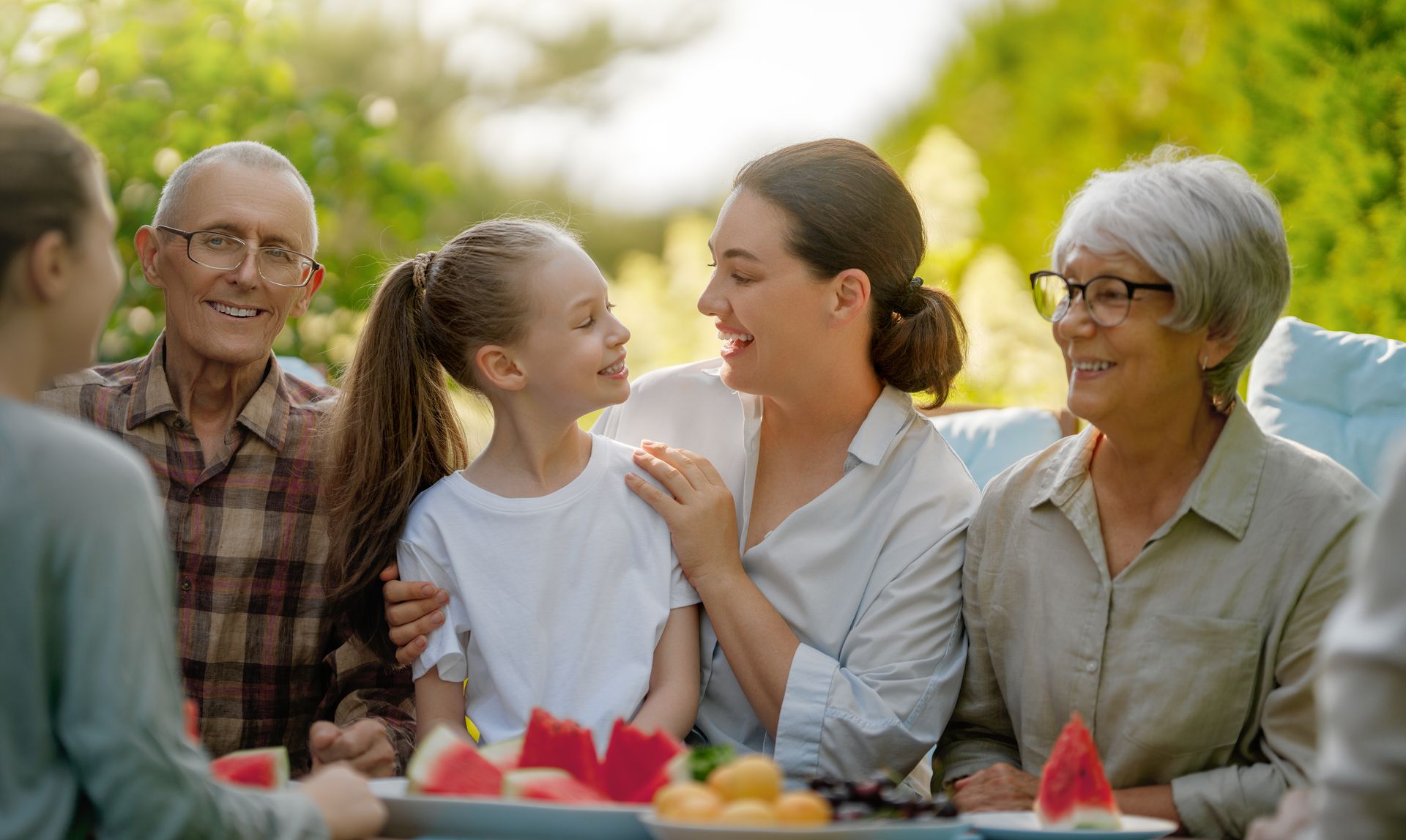 Family eating watermelon and smiling outdoors at a picnic table