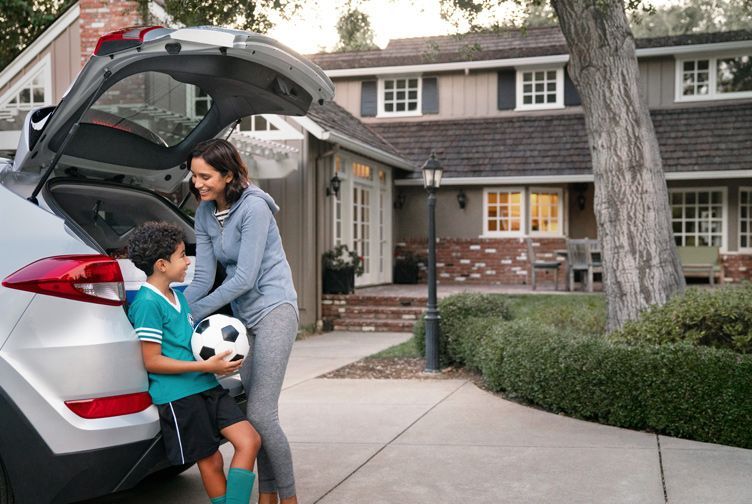 A woman and a boy are putting a soccer ball in the back of a car.