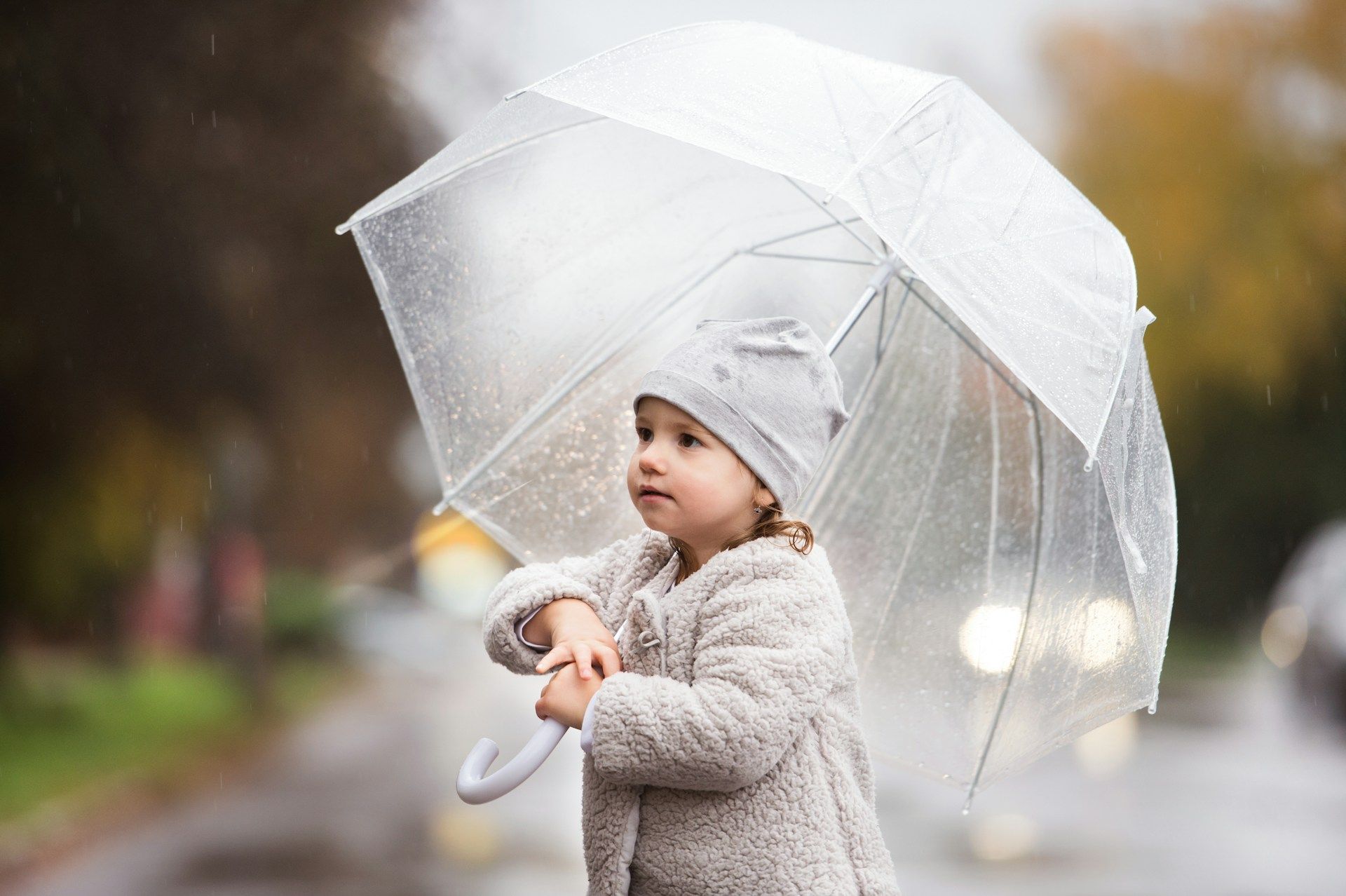 A little girl is holding a clear umbrella in the rain.
