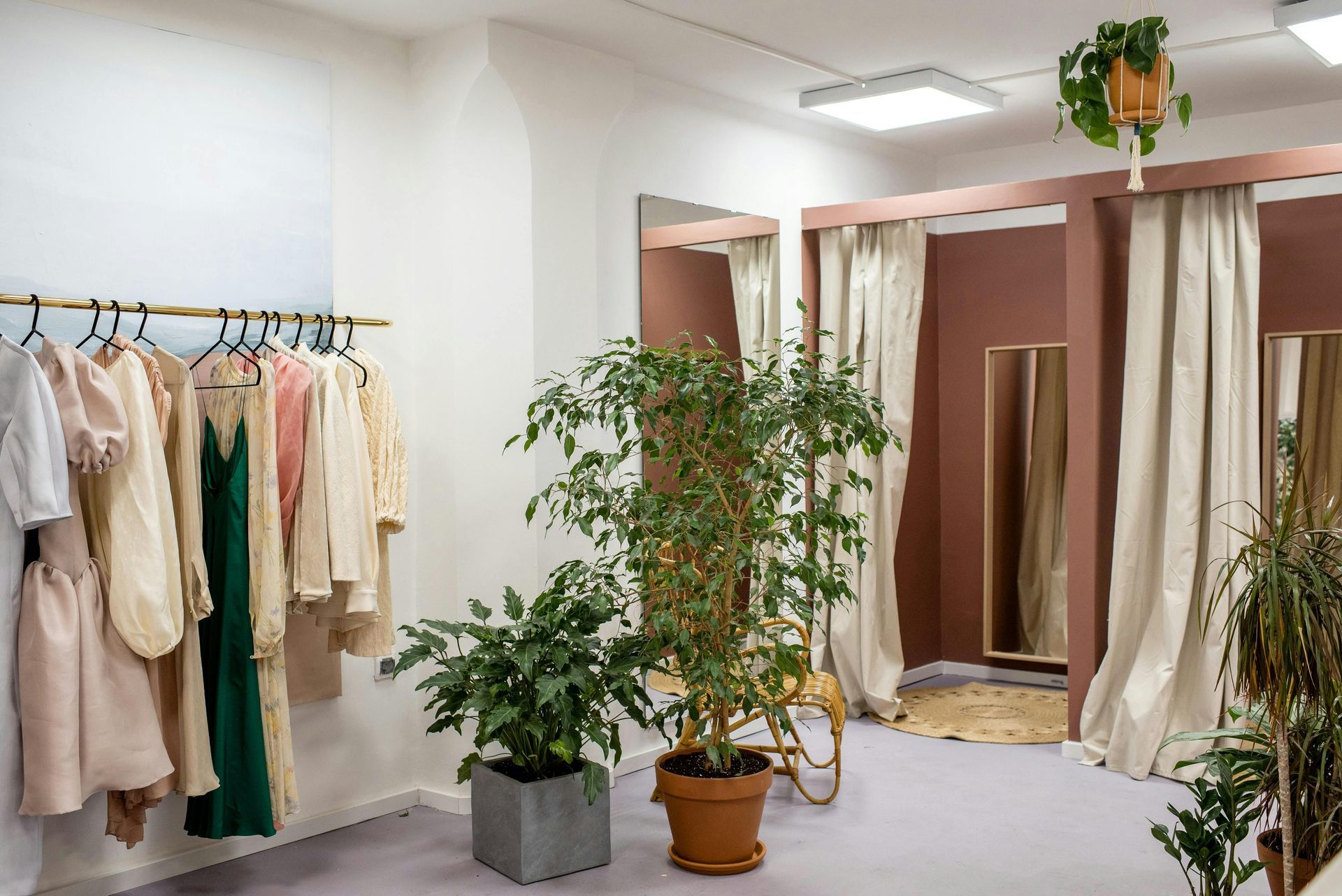 A dressing room with clothes hanging on racks and potted plants.