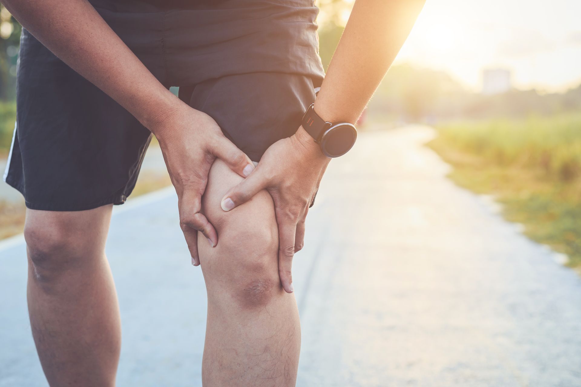 A man is holding his knee in pain while standing on a road.