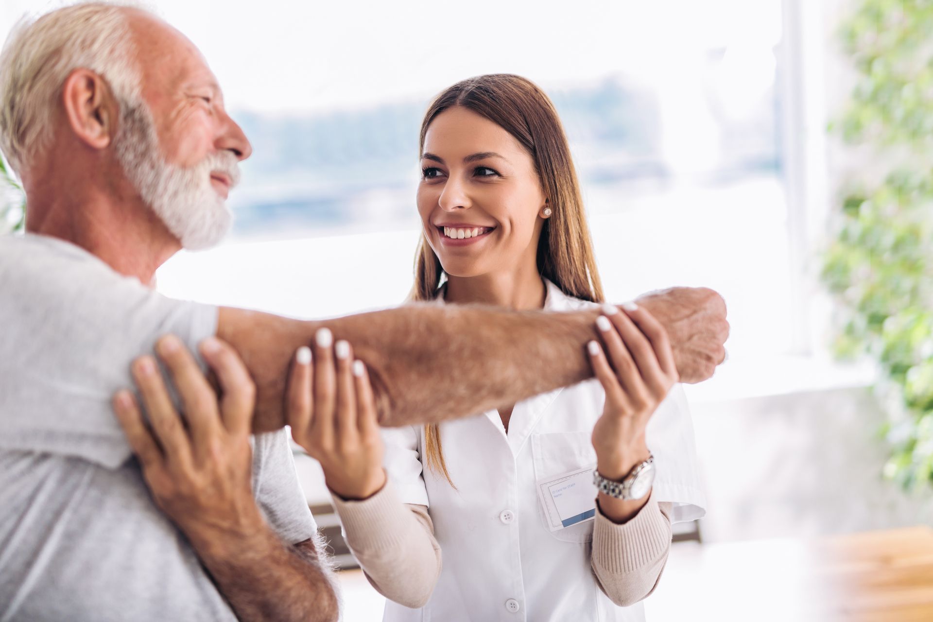 A nurse is helping an elderly man stretch his arm.