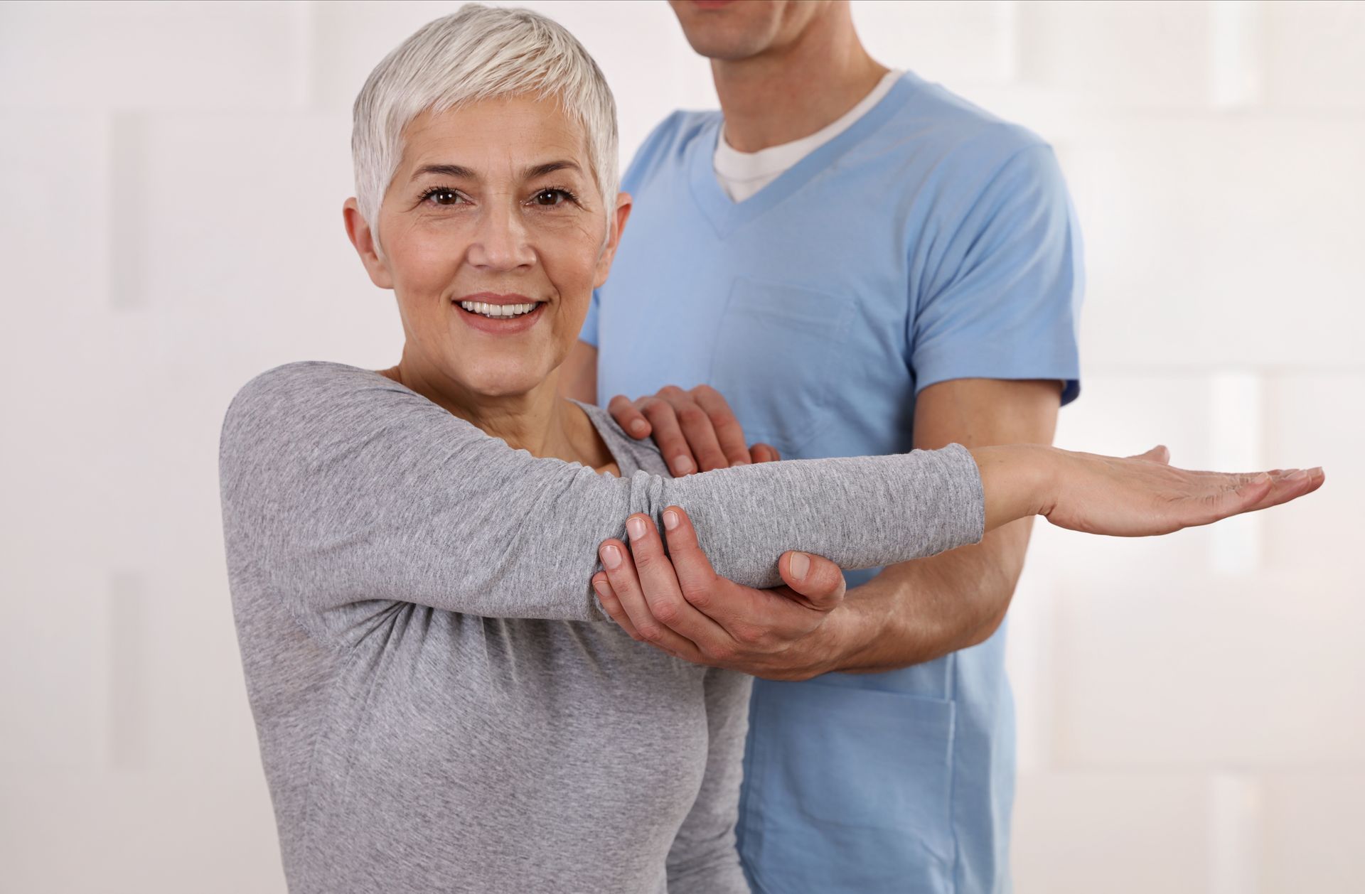 A man is helping an older woman stretch her arms.