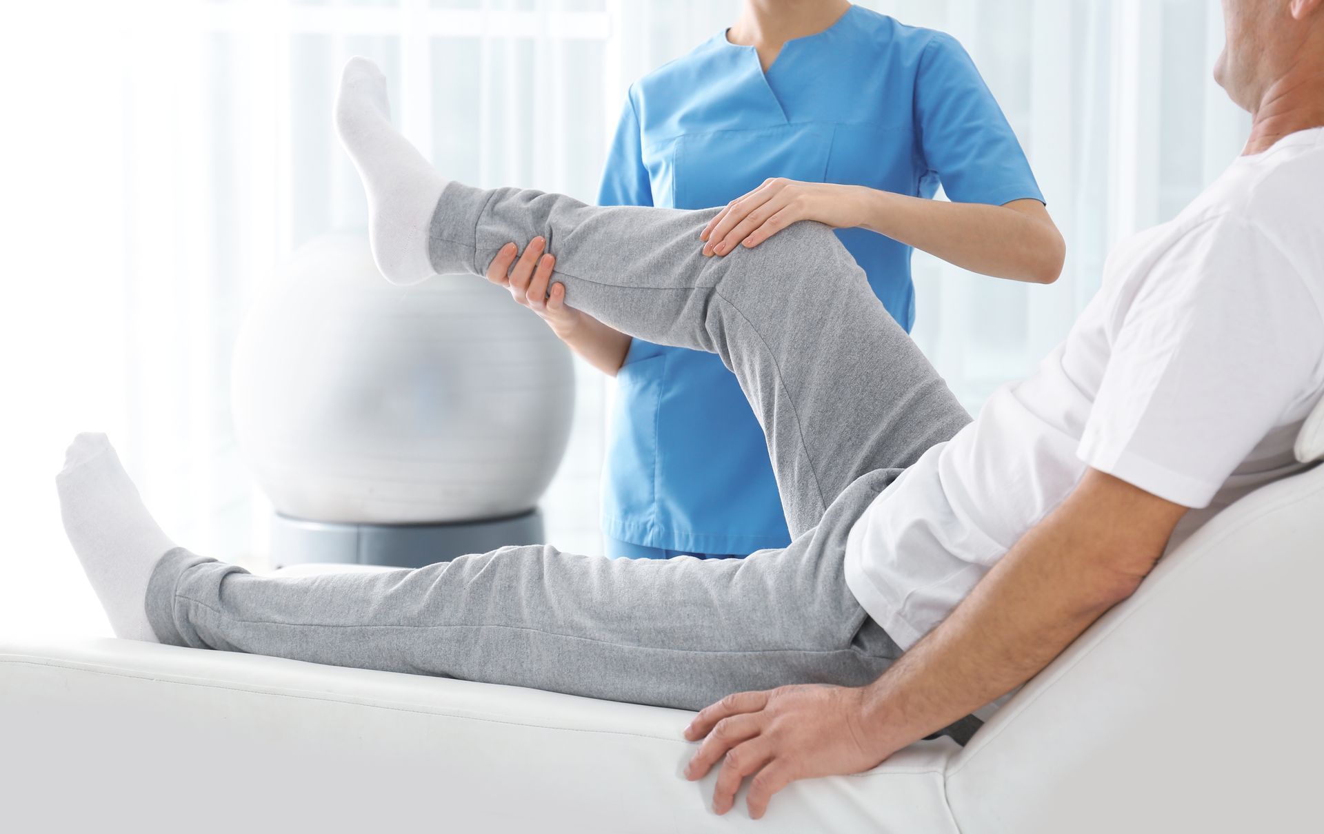 A nurse is helping an elderly man stretch his leg.