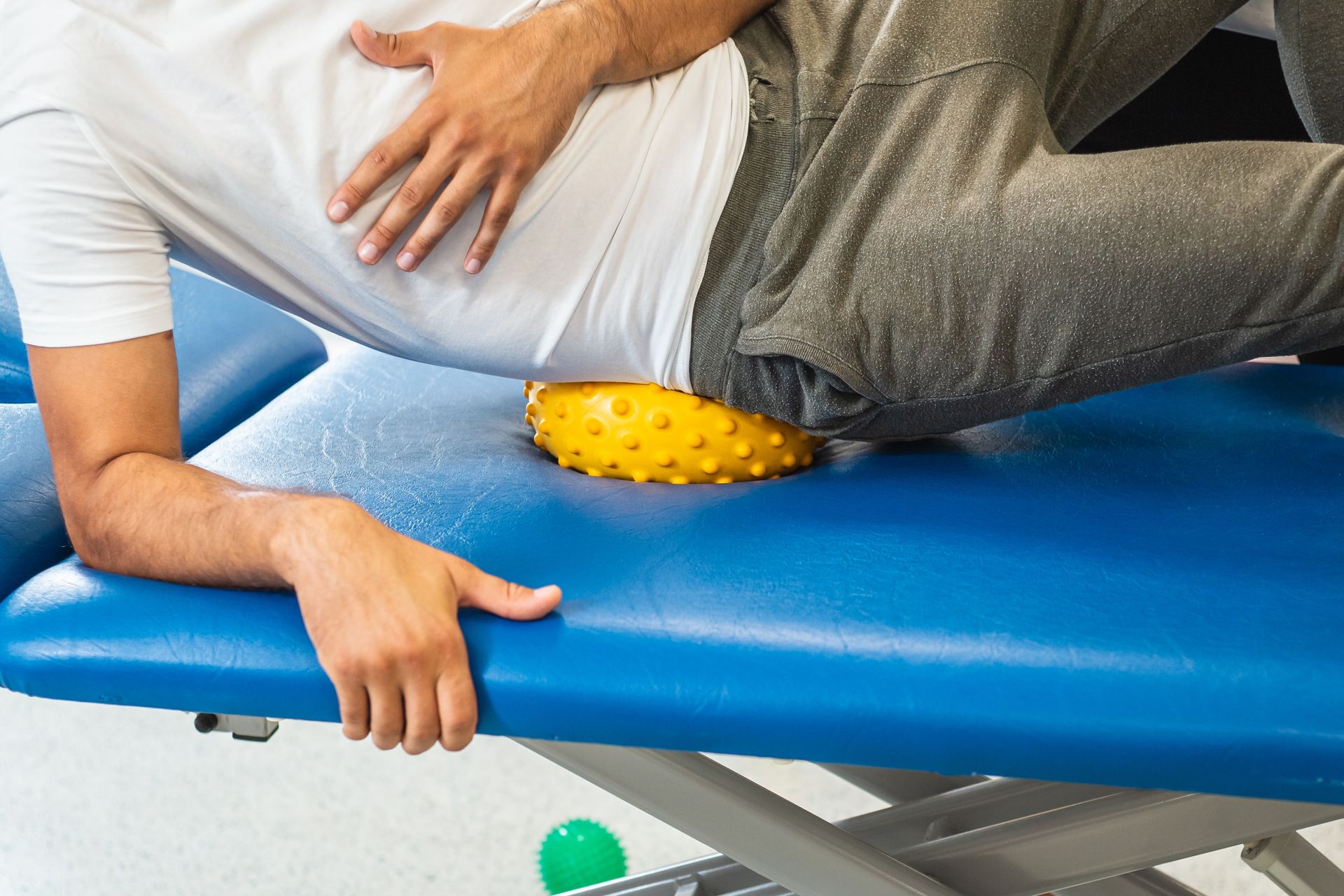 A man is laying on a blue table with a yellow ball on his back.