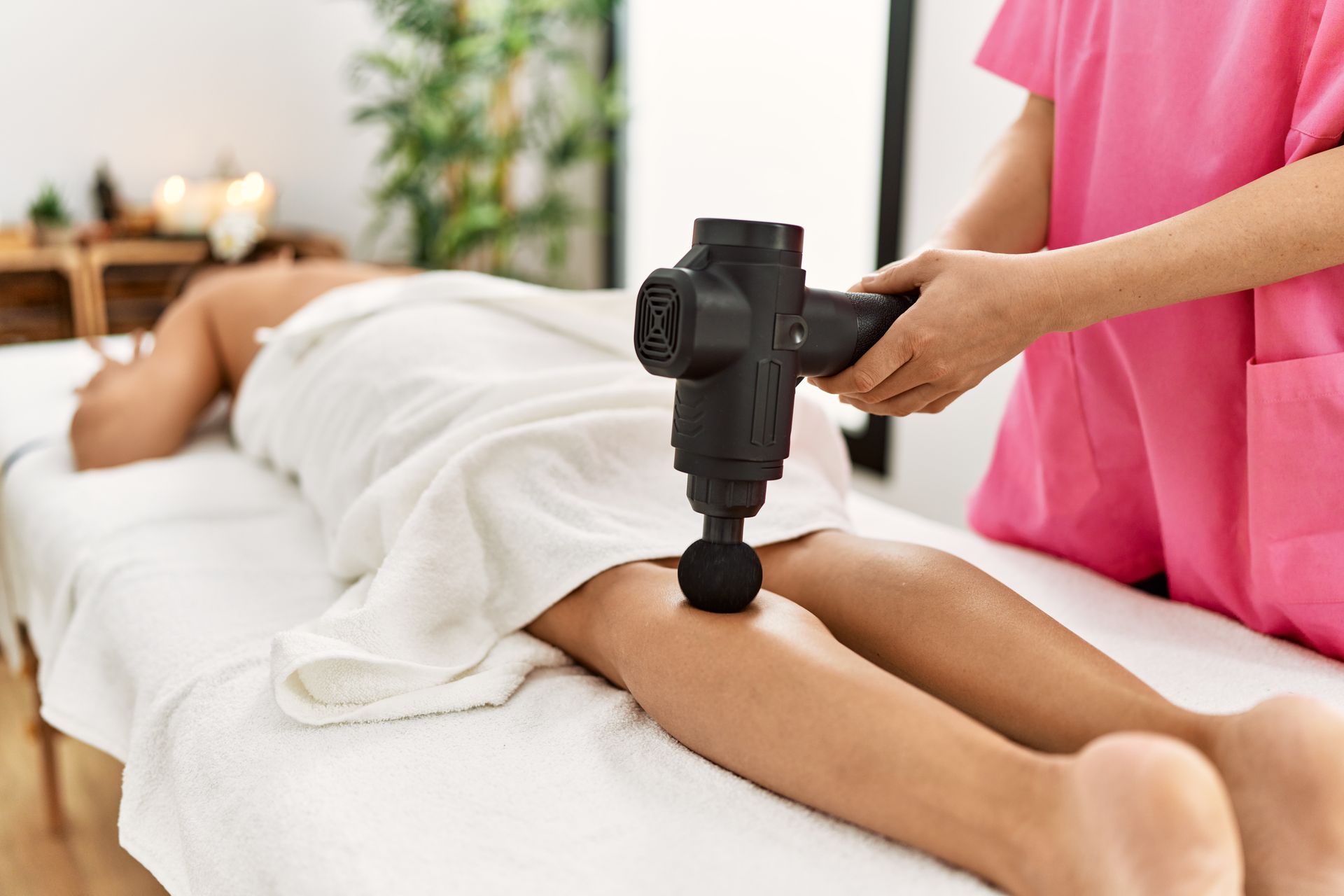 A woman laying on a massage table getting a percussion massage.