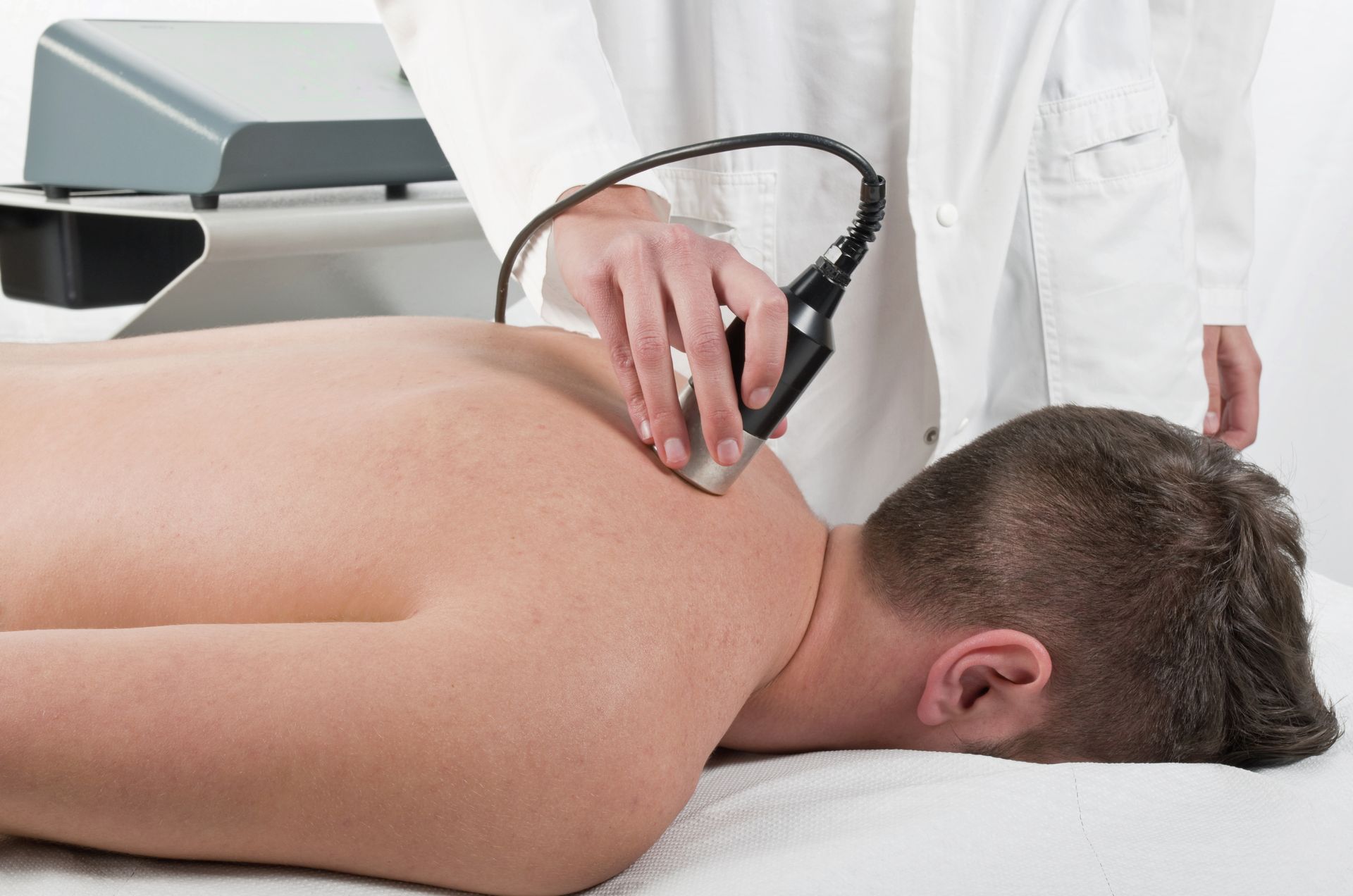 A man is laying on a bed getting a massage from a doctor.