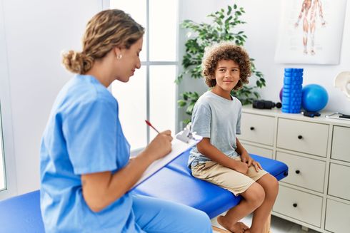 A nurse is talking to a young boy who is sitting on a table.