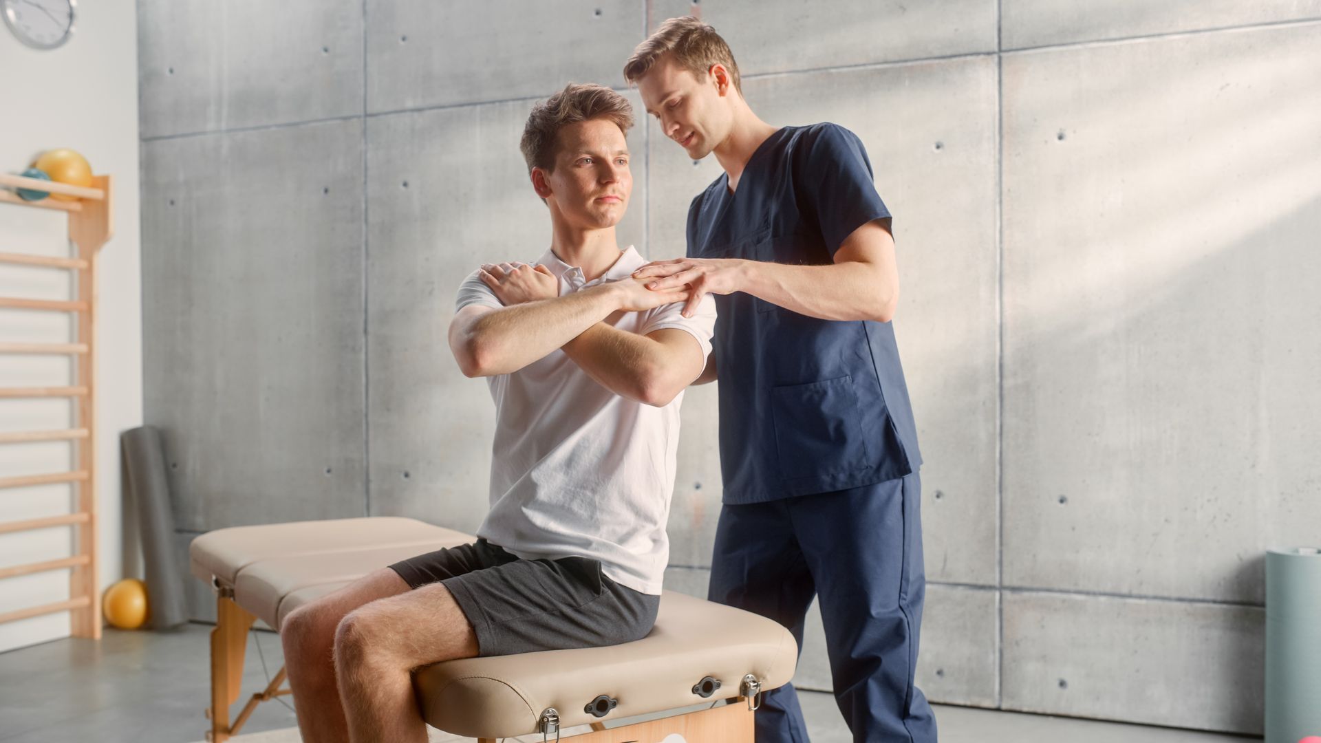 A man is sitting on a table while a doctor examines his shoulder.