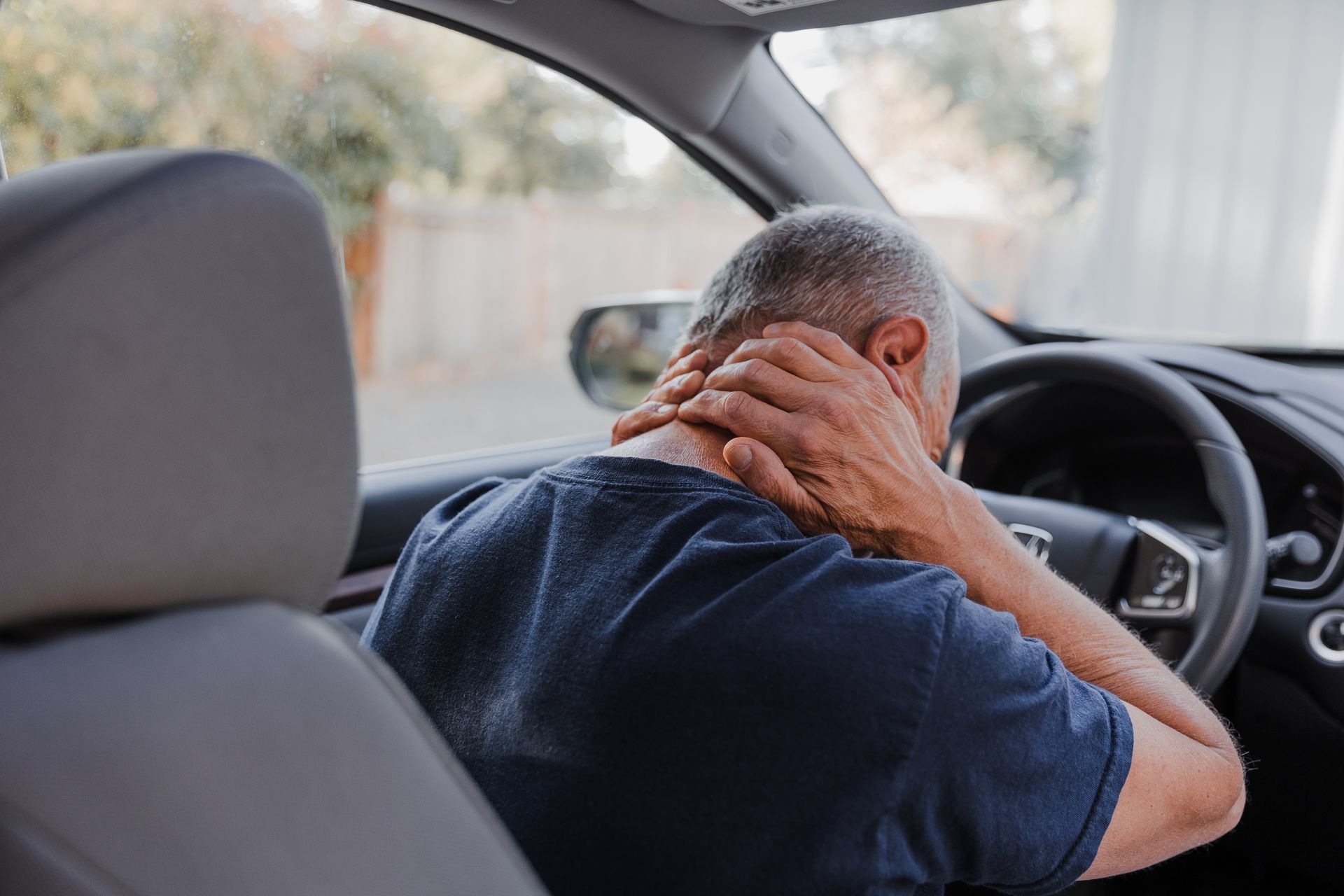 A man is sitting in the driver 's seat of a car holding his neck.