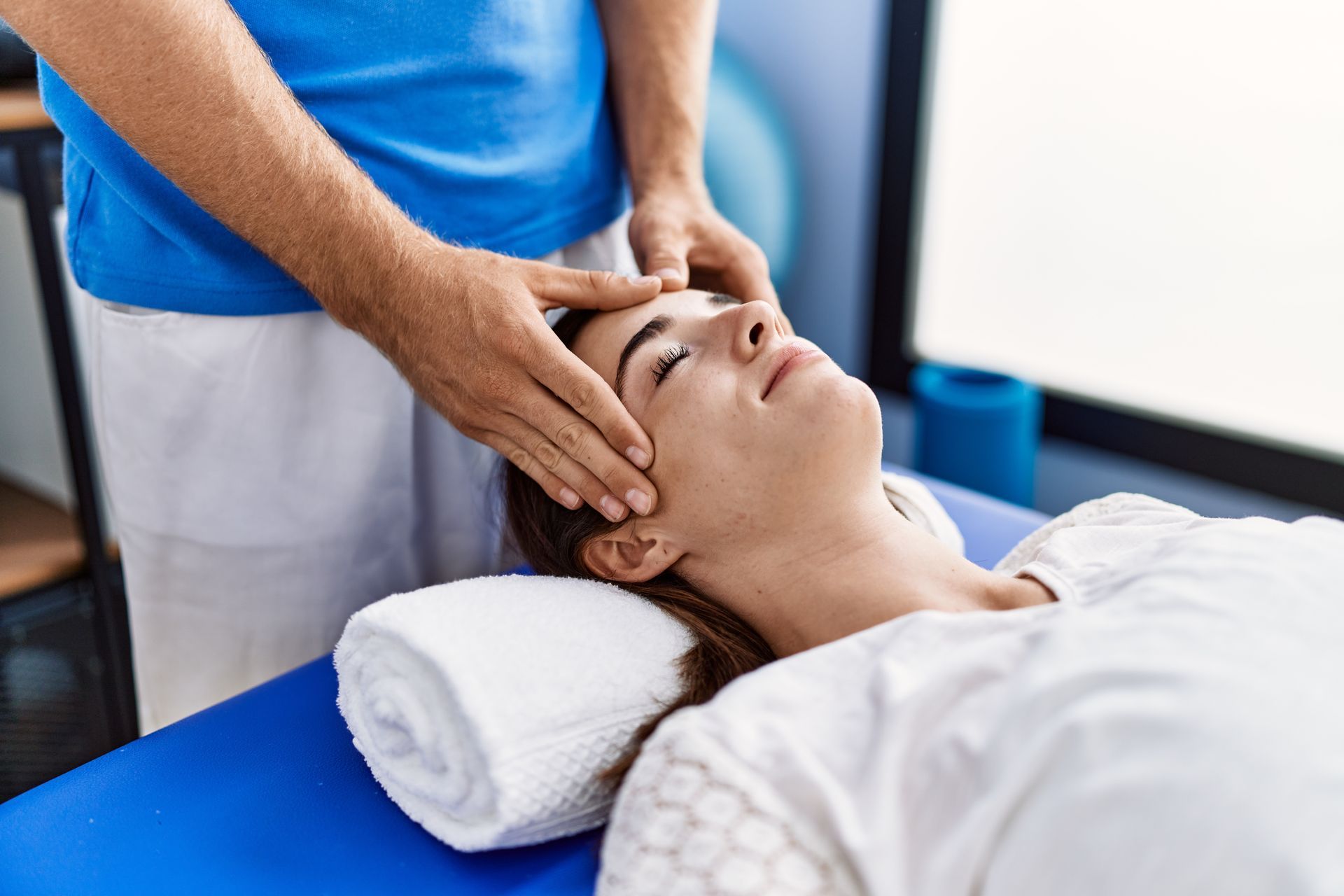 A woman is laying on a table getting a head massage from a man.