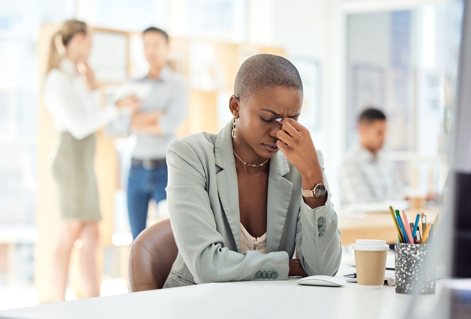 A woman is sitting at a desk with her hand on her forehead.