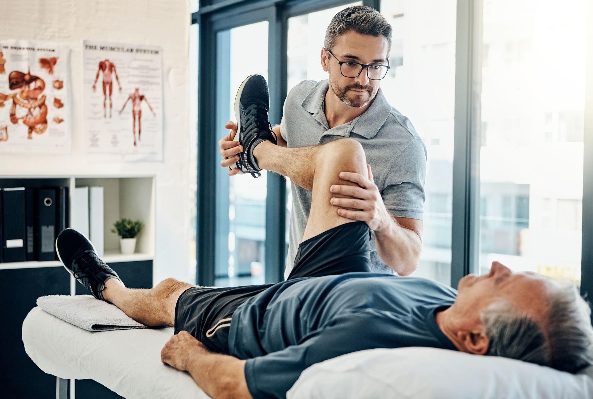 A man is laying on a bed getting his leg stretched by a doctor.