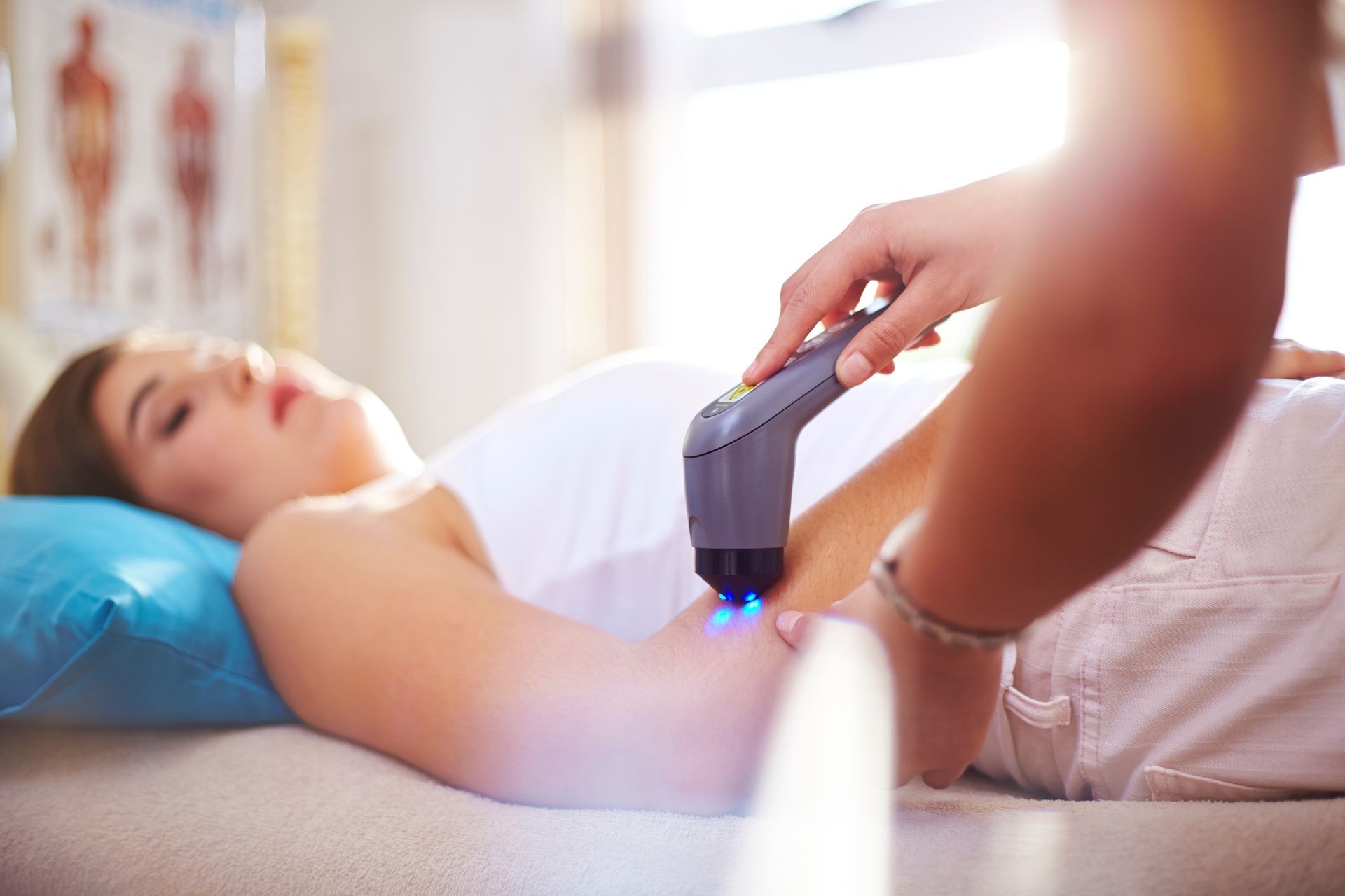 A woman is laying on a bed getting a laser treatment on her arm.